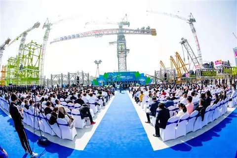 Massive greay and green flat top tower crane with rows of people in front at the launch
